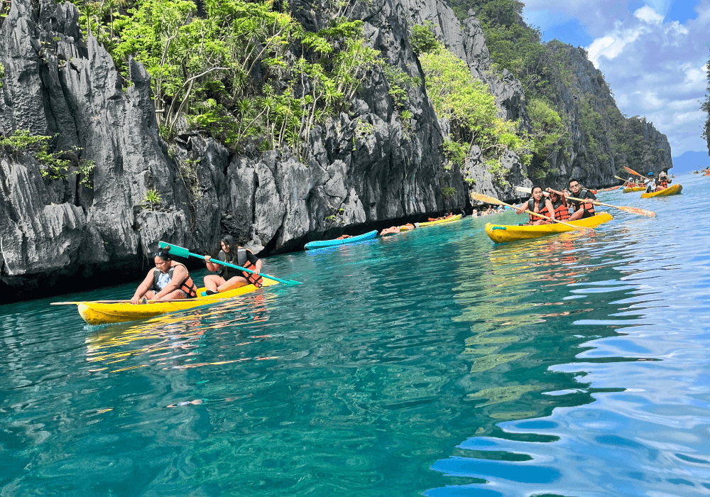 Travellers kayaking through clear blue water beside limestone cliffs.